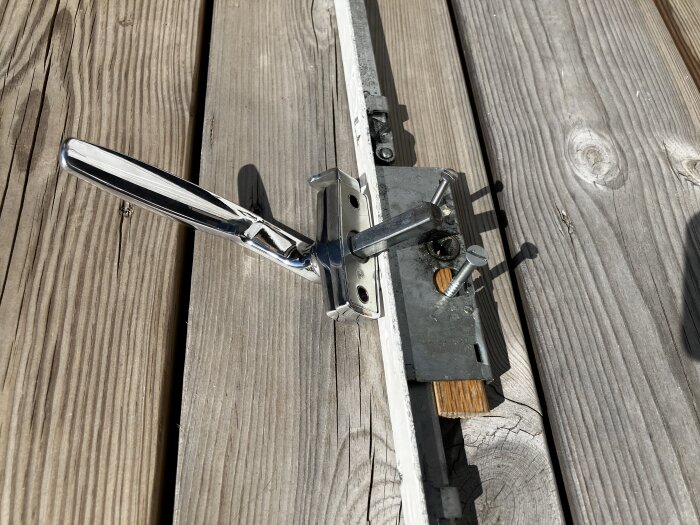 Dörrhandtag med spanjolett och modifierad låskista, inklusive två skruvar varav en i eklist samt detaljer på en träplanka i dagsljus.
