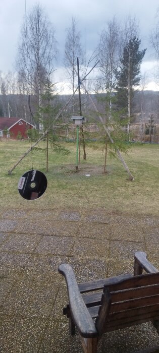 Trebening med tre 4 meter långa störar på en gräsmatta, används för att hänga upp älgar. I förgrunden en gammal bänk och träd i bakgrunden.