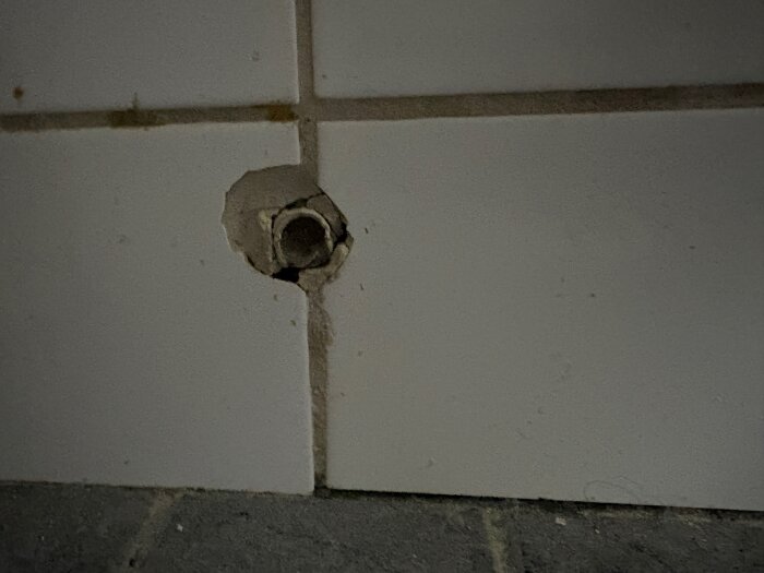 Hål i kakelvägg i ett badrum, synligt rör bakom plattan.