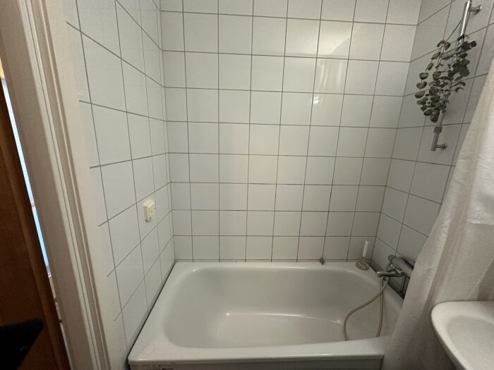 Badrum från 2003 med vitt kakel och badkar, visar hål i väggen under duschblandare; fråga om renoveringsbehov.