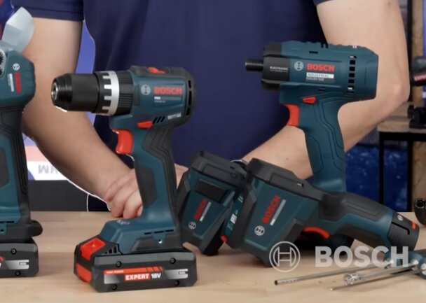 Verktyg från Bosch: en skruvdragare, en slagborr och andra elverktyg visas med en persons händer i bakgrunden, Bosch-logotyp synlig på verktygen.