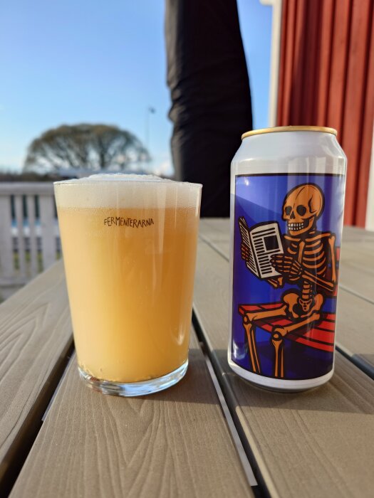 Ett glas öl från Fermenterarna och en ölburk med skelettmotiv på ett bord i solen.