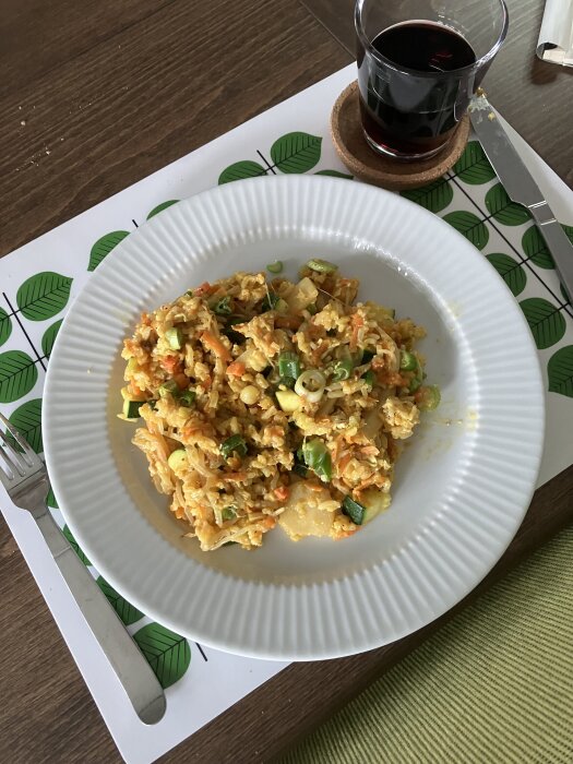 Tallrik med wok innehÄllande ingefÀra, vitlök, morot, ris, zucchini och rÀkor, bredvid ett glas mörk dryck.