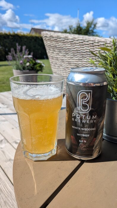 En ölglas och en burk Potum Brewery White Wedding witbier på ett trädäck i solen.
