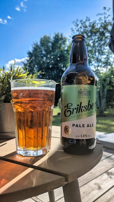 Flaska med Eriksberg Pale Ale och ett glas öl på ett bord utomhus.