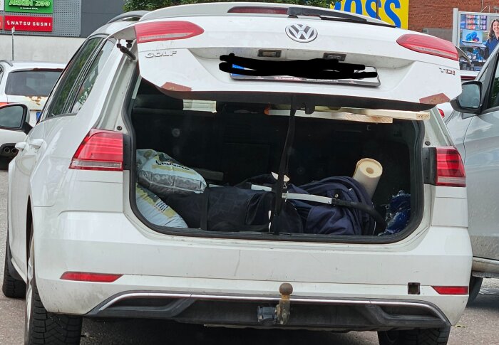Bakluckan på en vit bil är öppen och lastutrymmet är fyllt med paket, rullar och föremål som är ordentligt säkrade med remmar.