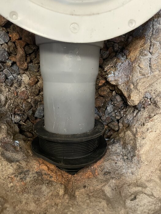 Grått plastavloppsrör installerat i en källarvägg, omgivet av sten och tätat med gummitätning.