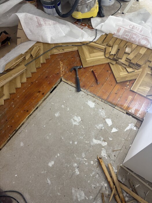 Golvrenovering pågår med borttagen parkett, verktyg och lösa träbitar. Synlig övergång mellan trä- och spånskiva.