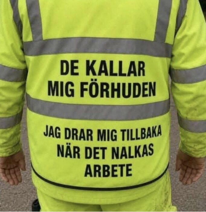 Arbetare i gul reflexväst med texten "De kallar mig förhuden, jag drar mig tillbaka när det nalkas arbete.