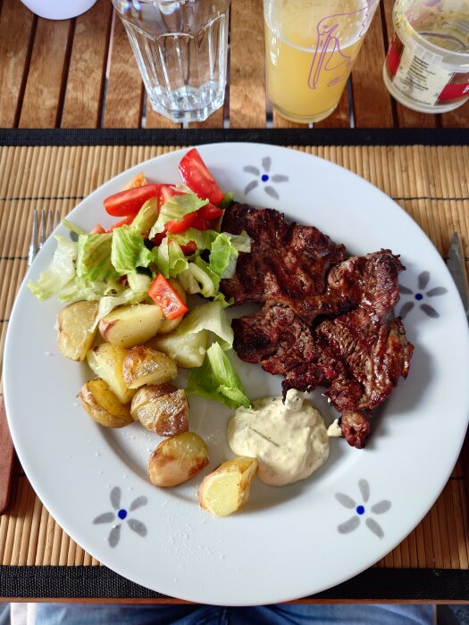 Grillad entrecote med ugnsstekt potatis, sallad och sås på en tallrik.