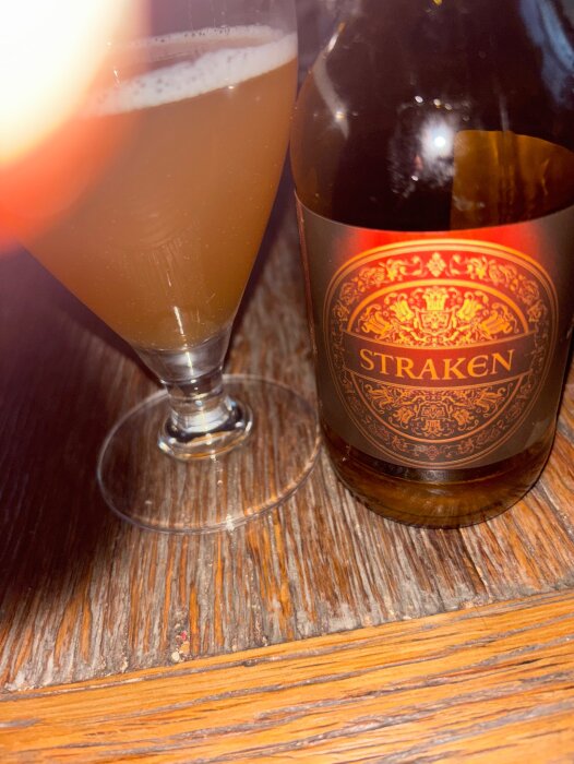 Flaska och glas med Straken öl från Bäckalunds gårdsbryggeri på ett träbord.