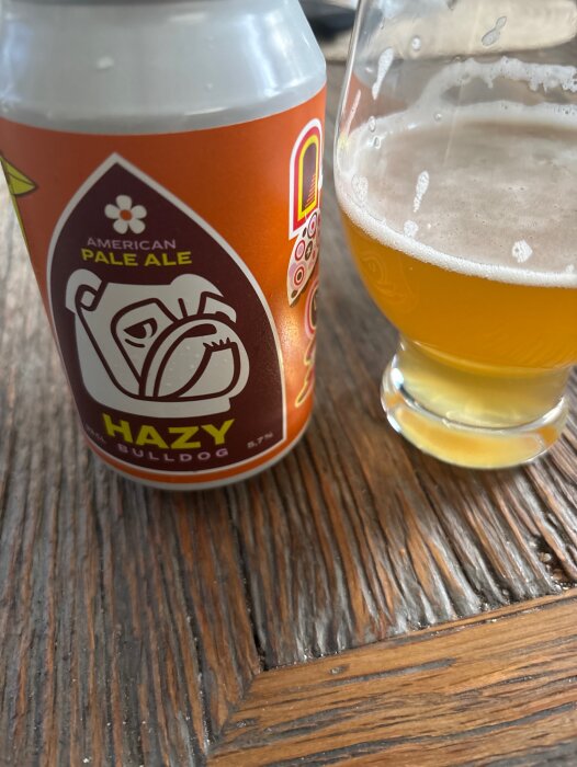 En burk American Pale Ale med etikett av en bulldog och glas med ljus öl på ett träbord.