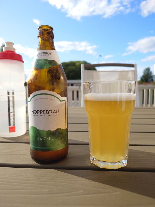 Flaska och glas med öl på ett bord utomhus en solig dag.