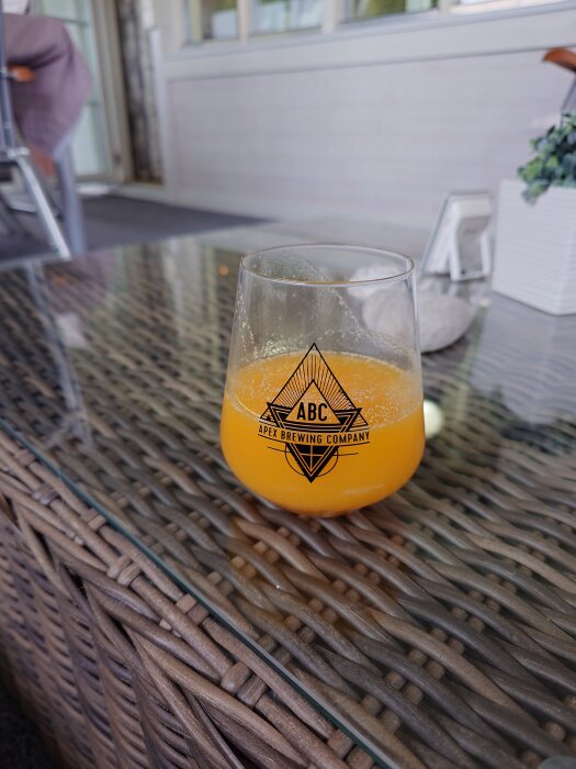 Bryggd av ananas, mango och cheesecake i ett glas från Apex Brewing Company på ett flätat glasbord.