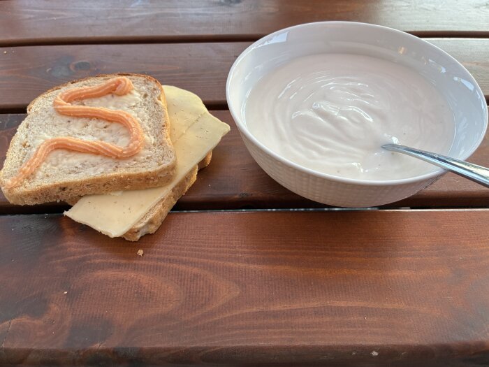 En skål med yoghurt och en smörgås med ost och kaviar på ett träbord.