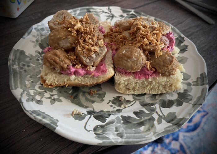 Köttbullsmacka med rödbetssallad och rostad lök på hembakad tekaka med rågsikt, serverad på en mönstrad tallrik.
