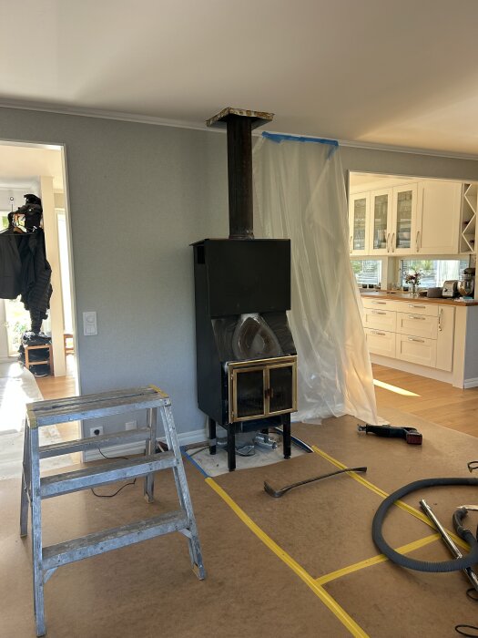 Rum under renovering med en installerad kakelugn, stege och verktyg på golvet.