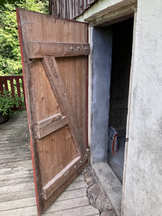 Öppen träport med rustikt utseende, visas från sidan, leder in till ett oisolerat rum med synlig säck på golvet.