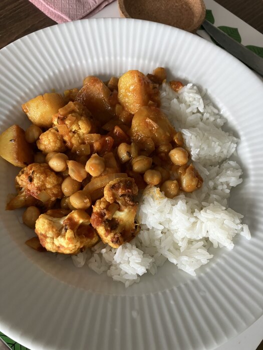 Tallrik med Aloo Gobi serverad med ris, synliga ingredienser inkluderar blomkål, kikärter och potatis.