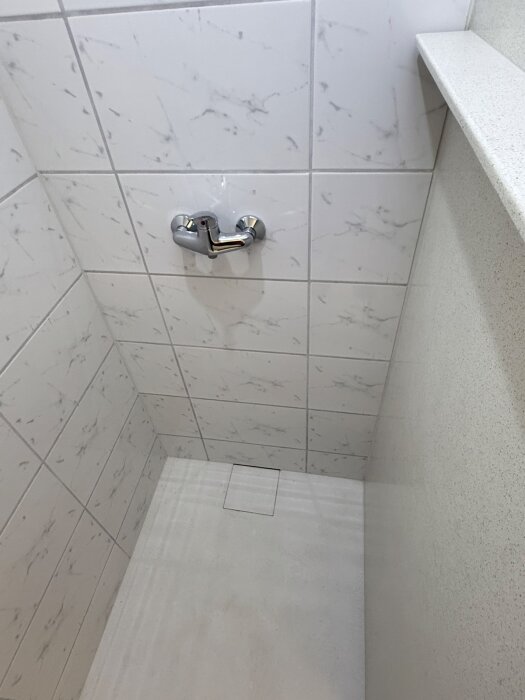 Duschhörna med marmorerade kakelväggar och nedsänkt golv med en stenplatta över brunnen. Modern och minimalistisk design.