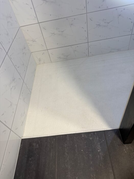 Nedsänkt duschgolv med vit stenplatta och marmorerade väggplattor i badrummet. Brunnen täcks av en tillskuren stenbit.