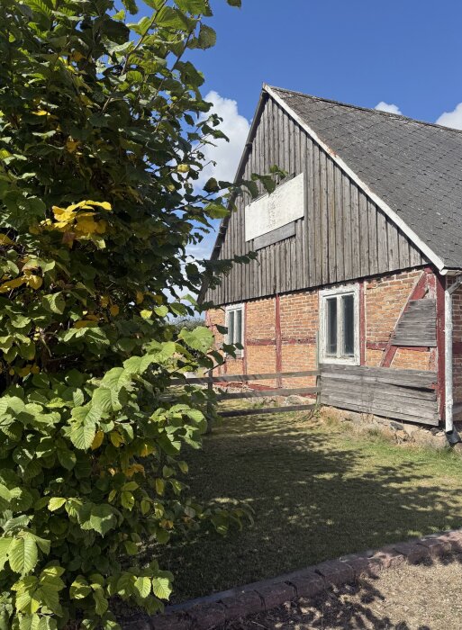 Rött tegelhus med trädetaljer och sluttande tak, omgiven av grönska under en klarblå himmel.