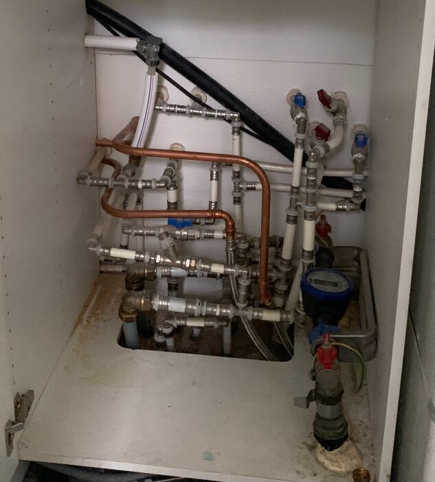 Vattenmätare och rörinstallation i ett skåp där bergvärme ska installeras. Rören är koppar- och metallfärgade med flera ventiler och kopplingar.