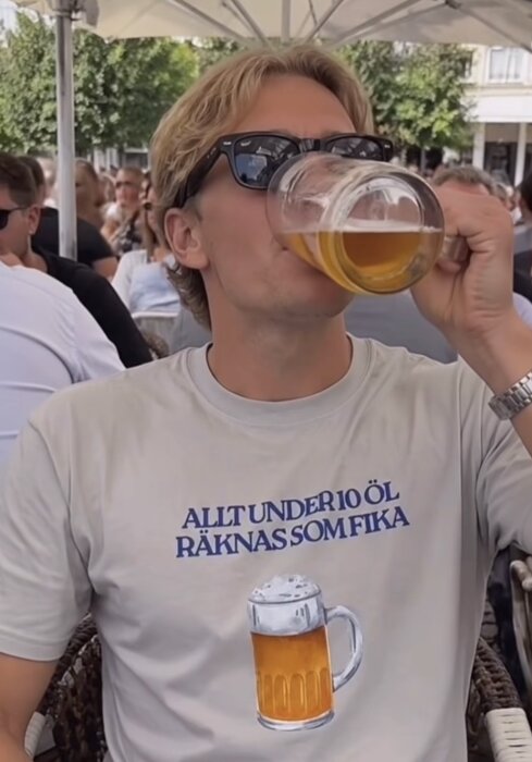 En person på en uteservering dricker öl, klädd i solglasögon och en t-shirt med texten "Allt under 10 öl räknas som fika" och en ölbild.