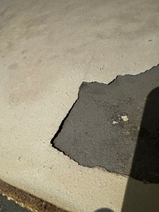 Underlag av vit filt/pappliknande material med en del avtäckt där plastmatta suttit fast på betonggolv, potentiell asbestmisstanke.