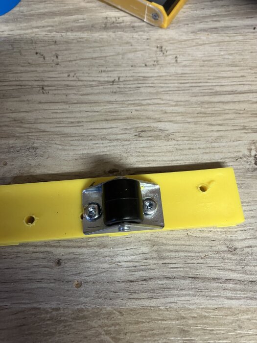 Självstängande myggnätsdörrjustering med gul och metallfärgad komponent monterad på en träyta.