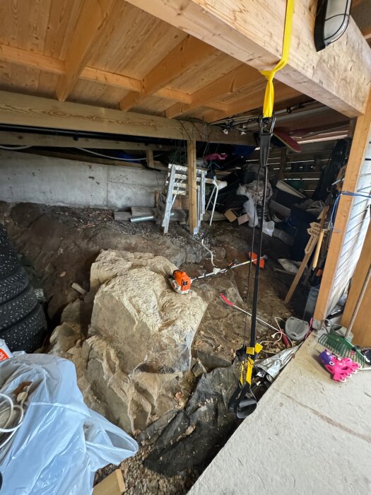 Bilden visar en bergklack under ett trädäck med diverse verktyg och material runtomkring, inklusive ett spännband, en såg, och ett gult rep.