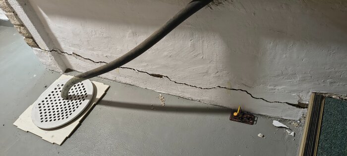Spricka i källarvägg med ansluten radonsugsslang och markskada, relaterat till frågor om sättningar i äldre hus.