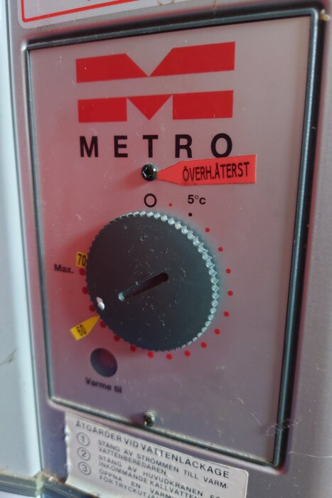 Termostat för varmvattenberedare av märket Metro, med ratt för temperaturinställning och etikett för överhettningsåterställning.