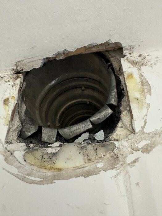 Ventilationskanal med delvis borttagen gips och spackel, upptäckt undertak och en regel ovanpå kanalen. Öppning visar rörens diameter Ø100.