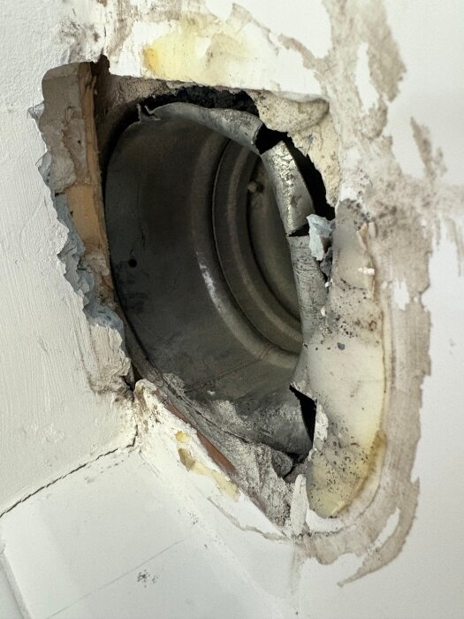 Ventilationskanal delvis täckt av undertak, synligt efter borttaget gips/spackel. Regel går över toppen av kanalen med synlig skadad kant.