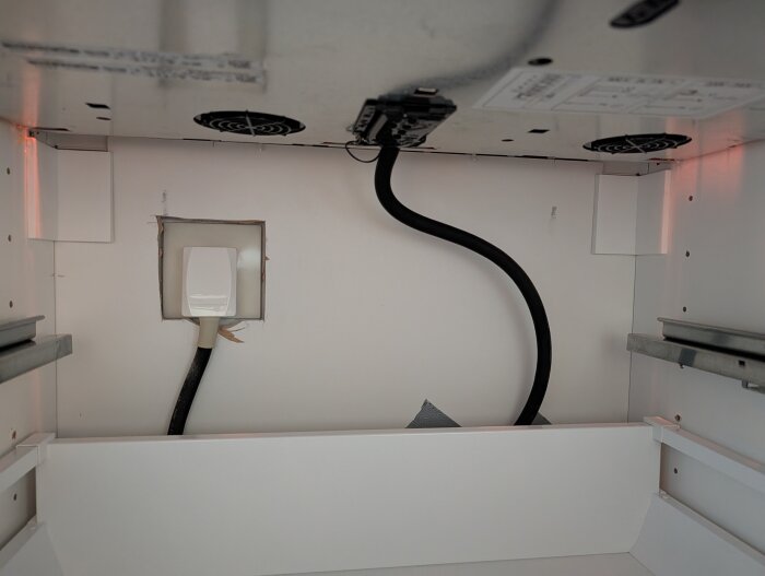 Elektrisk installation under spis med synliga kablar och uttag, potentiell plats för anslutning av förgreningsdosa för vinkyl.