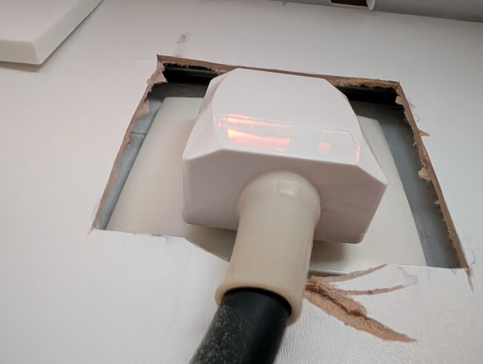 Uttag och elkabel synliga bakom en uppbruten yta i köksväggen under en spis, potentiellt för vinkylens installation.