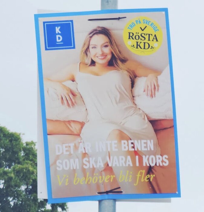 En valaffisch med person som ligger på en soffa, omgiven av texten "Vi behöver bli fler" och "Tro på Sverige, rösta KD".
