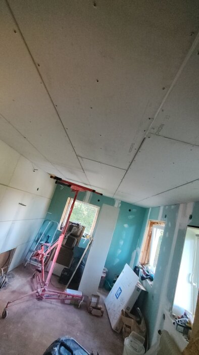 Tak med gipsplattor i ett renoveringsprojekt i kök, gipslyft syns i mitten av rummet, turkosa väggar och byggmaterial runtom.