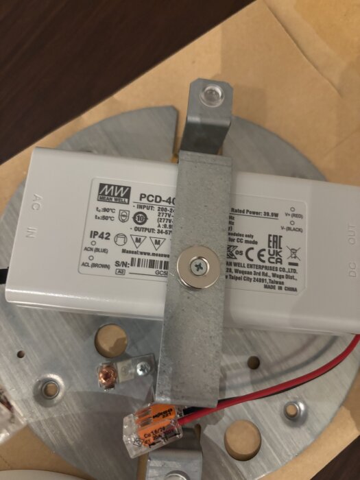 Lampfäste med installationskomponenter och kopplingsbox för Stilnovo lampa visas, monterat på en metallplatta med synliga kablar och skruvar.