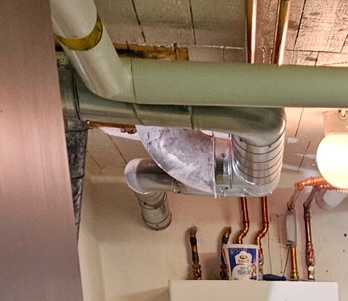 Ventilationssystem med silverfärgade rör och kopparrör mot en vit vägg, del av ett renoveringsprojekt.