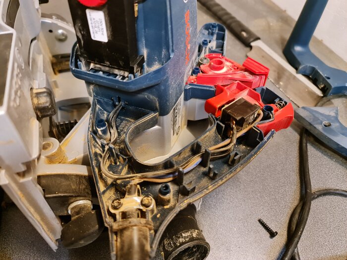Öppen sänksåg Bosch GKT 55 GCE visar interna komponenter, med kabeldragning och delar av varvtalsregulatorn synliga, tillsammans med en svart skruv i förgrunden.
