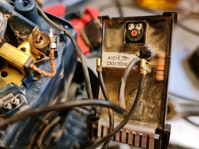 Närbild av en del av en sågs varvtalsregulator med kretskort och kablar, misstänkt svullen kondensator, etikett med "230V 50Hz" text.