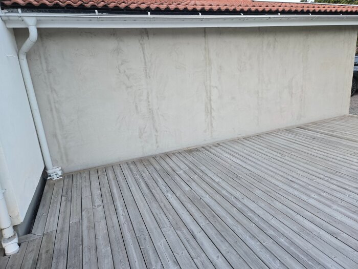 Putsad garagevägg med vertikala sprickor, omgiven av trätrall och vit stuprör. Taken är täckt av röda takpannor.