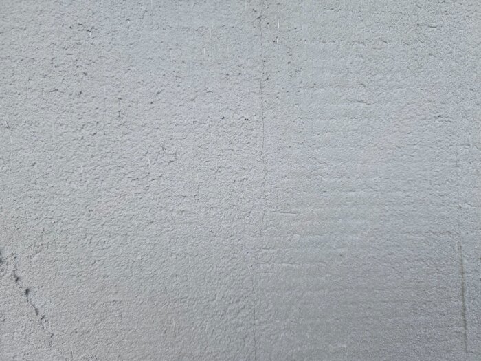 Putsad garagevägg med synliga vertikala sprickor efter applicering av fibernät och puts. Sprickorna orsakade av temperaturförändringar och friggolitsunderlag.