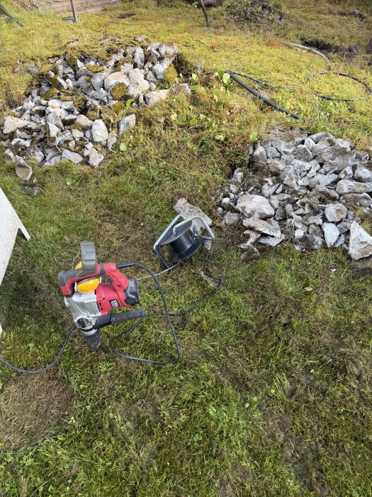 En gräsmatta med högar av spräckt sten och en borrmaskin, pågående arbete för att blottlägga berg.