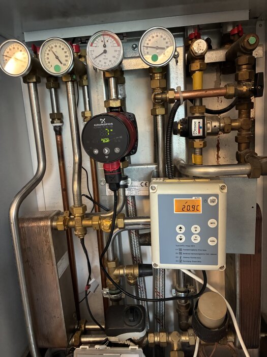 Värmesystem med rör, mätare och en elektronisk kontrollpanel som visar temperatur 20,9°C.
