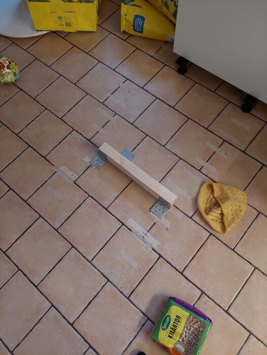 Klinkergolv med träregel och byggmaterial i kök, gula förpackningar och kikärtor synliga.