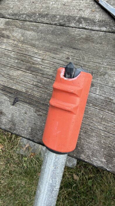 Röd, avtagbar plastdel på metallstång liggande på träbord, diskuteras angående demontering eller reparation.