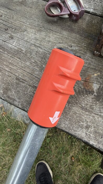 Röd del på metallrör med vit pil på, ligger på träbord med sax bredvid. Användare undrar hur man demonterar för reparation.